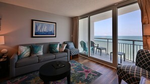 En moderne stue med en grå sofa, et rundt sofabord og et stort vindue med udsigt til havet.