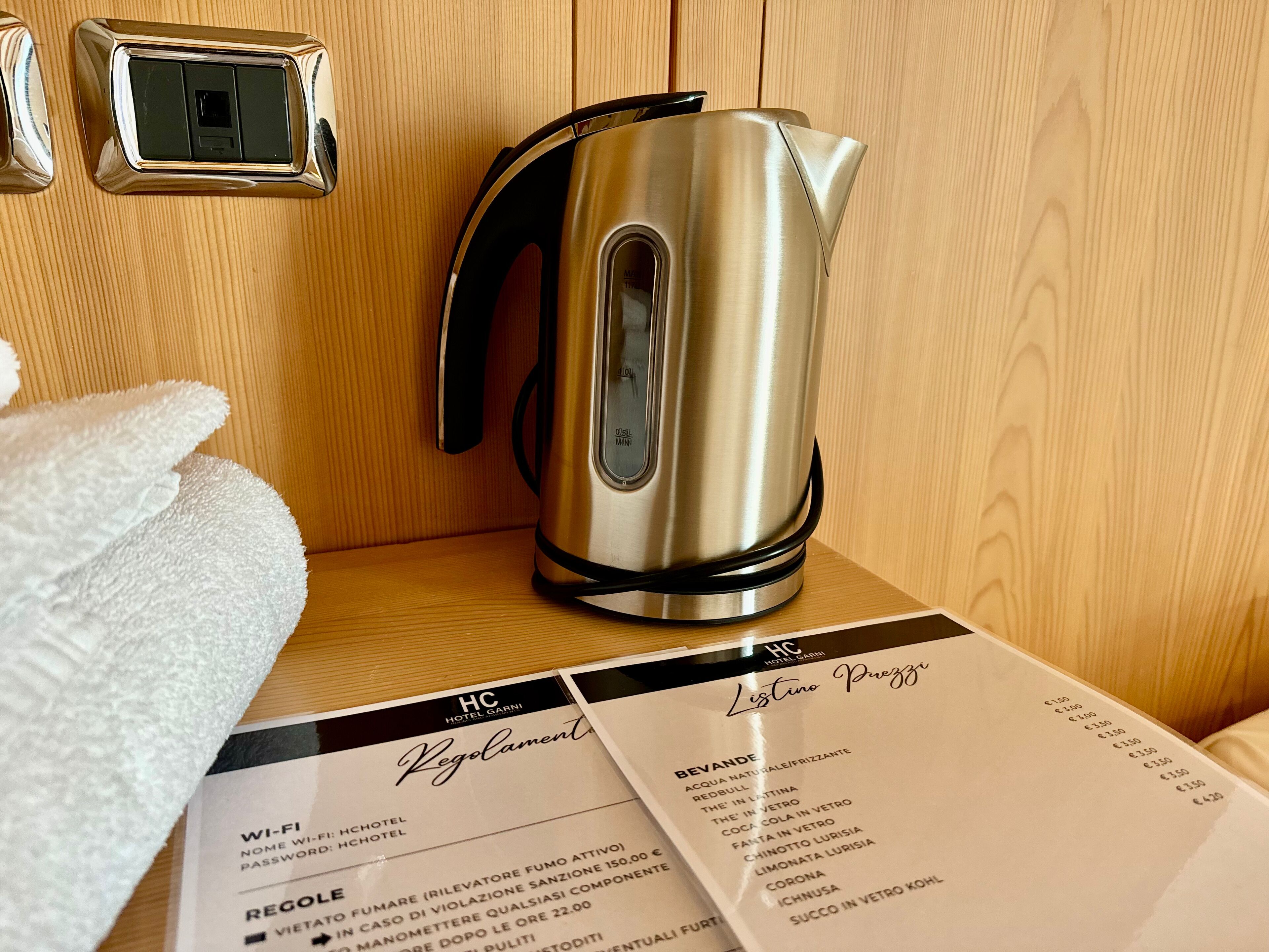 A metallic kettle on a wooden surface with a menu and a Wi-Fi sign.
