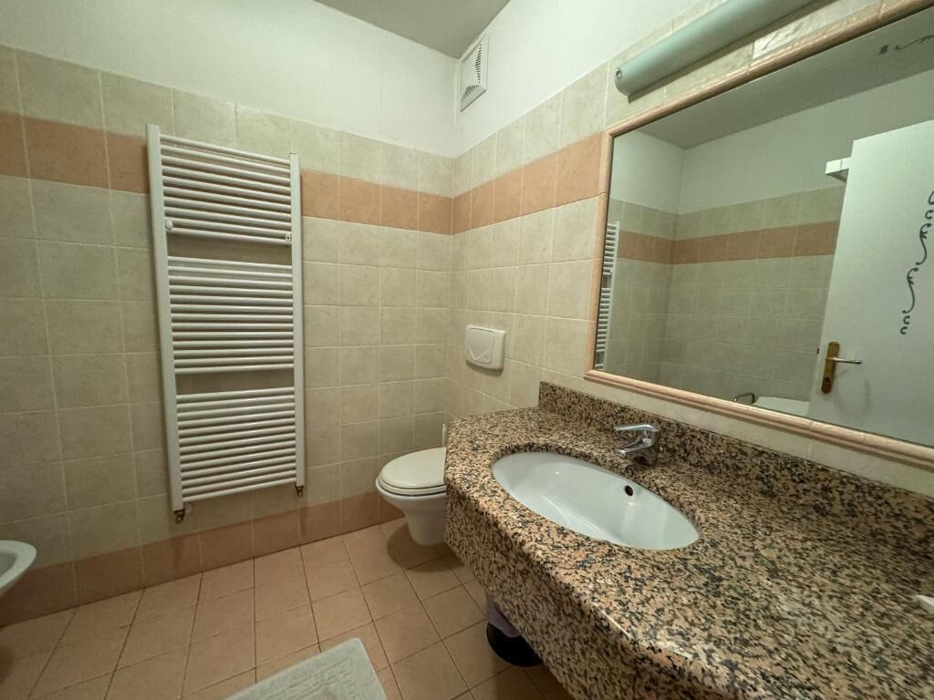 A bathroom with a granite sink, a white toilet, and a towel rack.