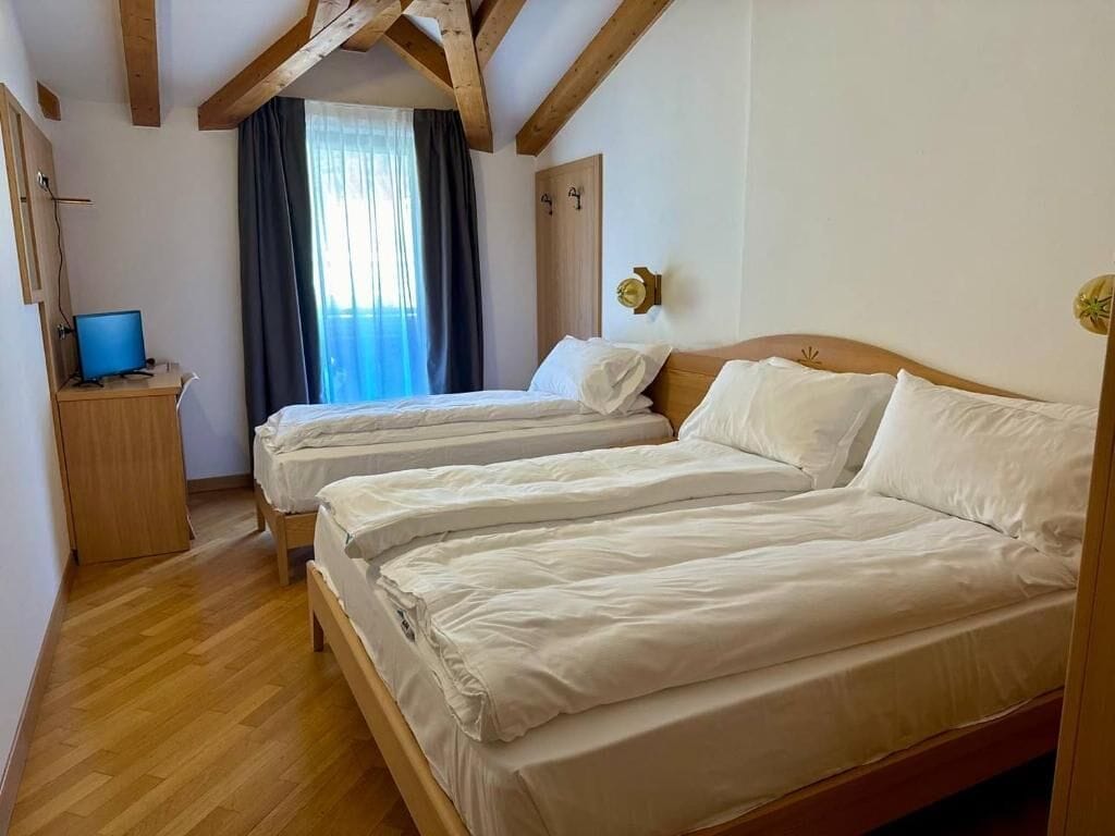 Quarto com duas camas, uma escrivaninha com computador e uma janela com cortinas.