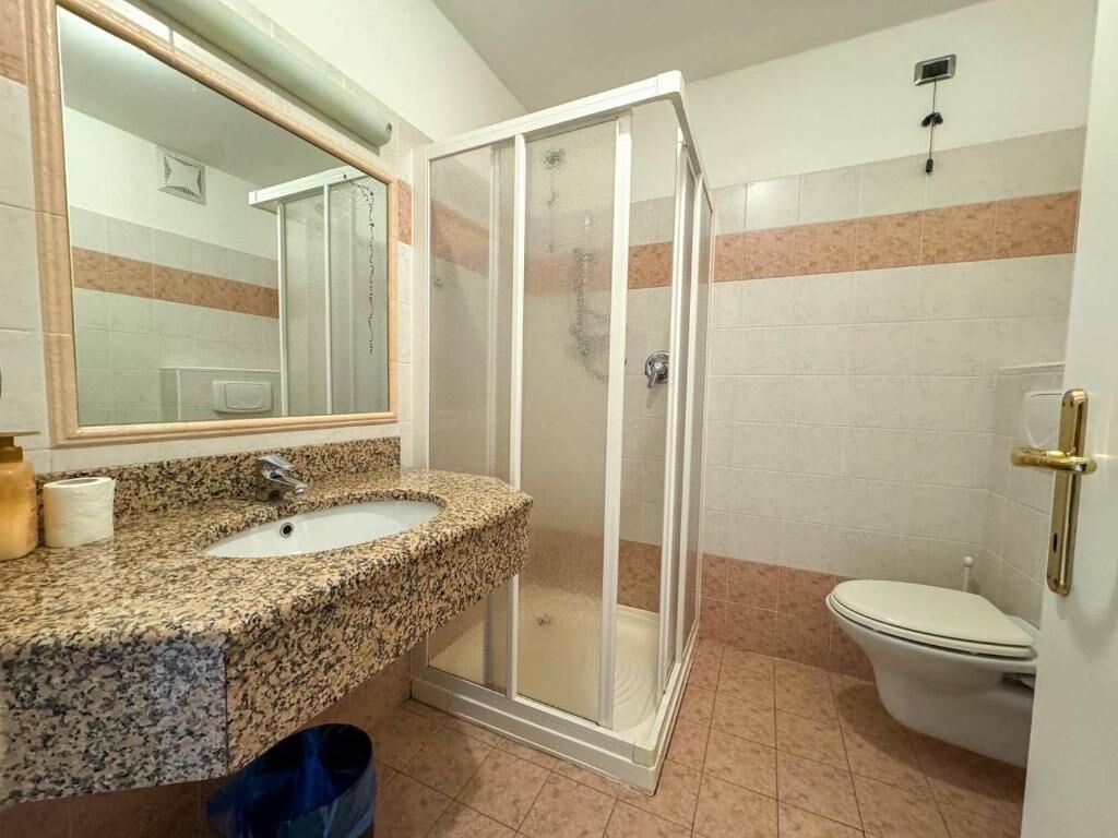 Un baño con lavamanos de granito, cabina de ducha con mampara de vidrio y un inodoro.