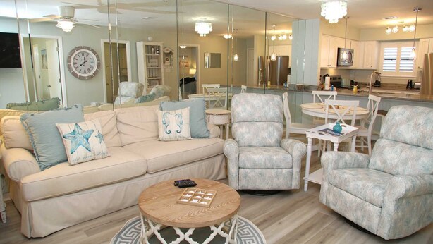 A modern living room with a beige sofa, two armchairs, a coffee table, and a dining area with a chandelier. - Completely Renovated Jan 2026 - Bring the Boat! (Orange Beach)
