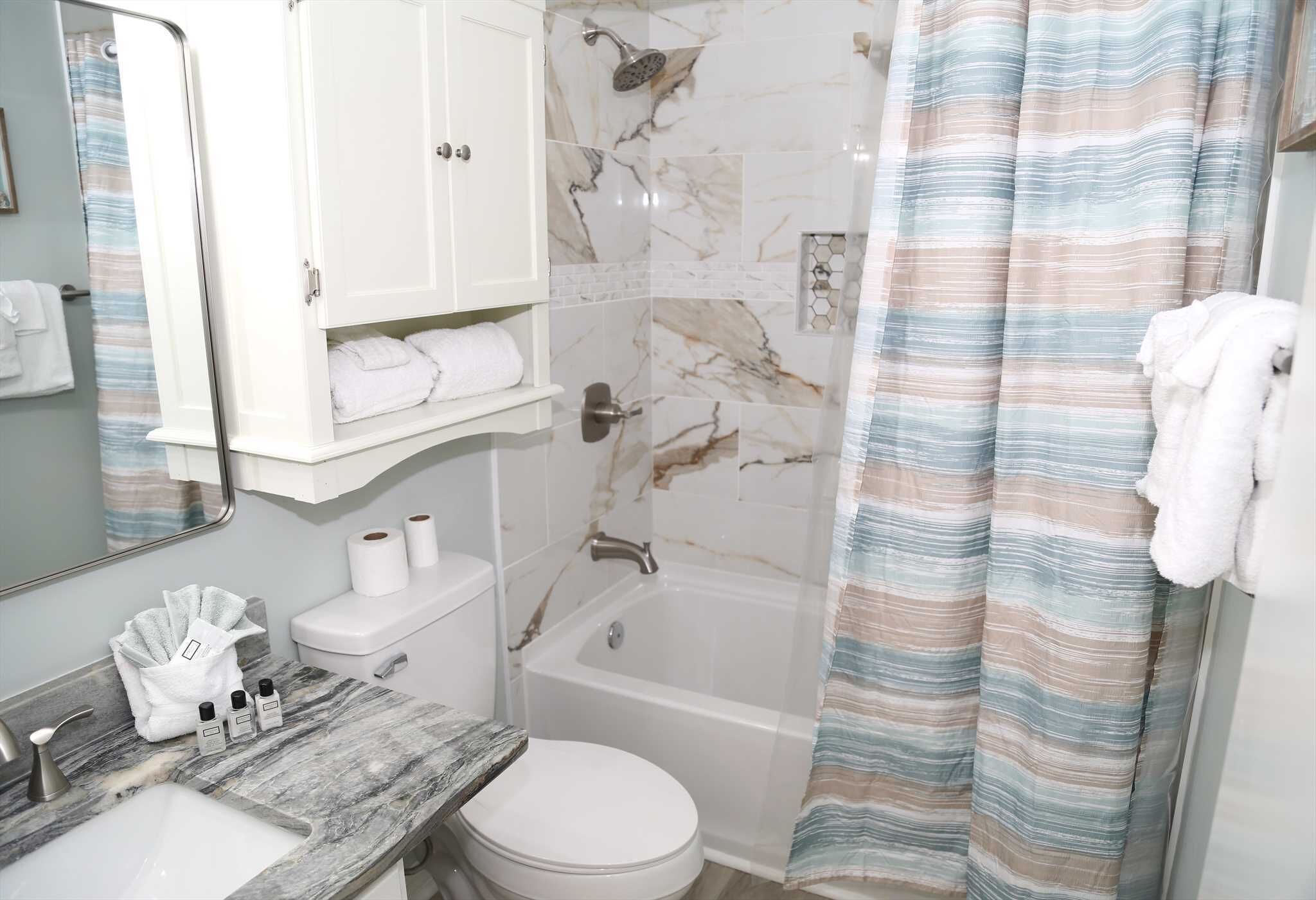 A bathroom with a marble sink, toilet, and bathtub. There is a shower curtain, a towel rack, and a mirror.