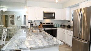 A modern kitchen with white cabinets, a stainless steel refrigerator, a built-in microwave, and a granite countertop. - Completely Renovated Jan 2026 - Bring the Boat! (Orange Beach)