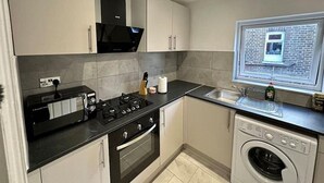 A modern kitchen with a built-in oven, stove, and microwave, a washing machine, and a window with a view of the outside. - 3 bed Hackney/Harringay Flat (London)