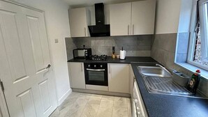 A compact kitchen with a gas stove, oven, microwave, and a sink. - 3 bed Hackney/Harringay Flat (London)