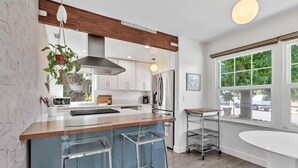 A modern kitchen with a wooden island, bar stools, a stainless steel refrigerator, and a large window providing a view of the outdoors. - *NEW San Diego Home-Private Hot Tub & Views+Pet (San Diego)