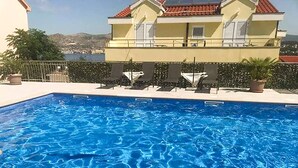En swimmingpool med solstolar och utsikt över en byggnad med ett rött tegeltak.