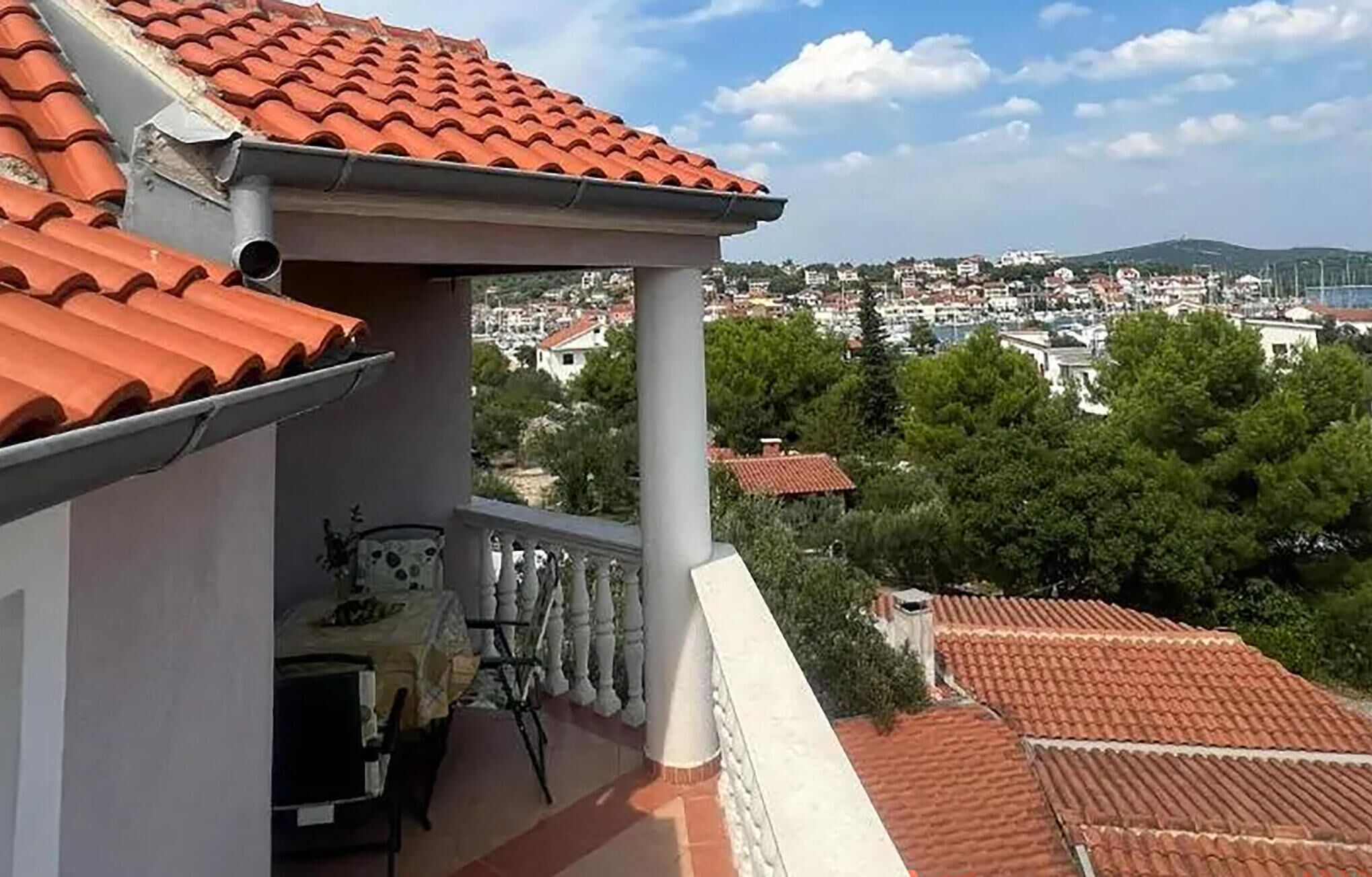 Een balkon met een betegeld dak, met uitzicht op een woonwijk met huizen en bomen.