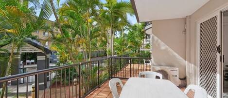 A balcony with a white table and chairs, surrounded by a metal railing.