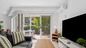 A modern living room with a sofa, coffee table, TV, and sliding glass doors leading to a balcony with outdoor furniture. - Broadwater Waterfront Balcony near Sea World (Labrador)