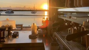 A kitchen with a coffee machine, a window overlooking a marina with boats, and a view of the sunset. - Broadwater Waterfront Balcony near Sea World (Labrador)