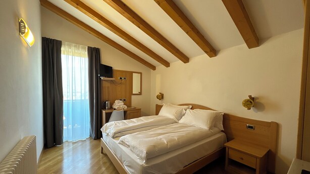 Ein Schlafzimmer mit einem hölzernen Bett, Nachttischen, einem Schreibtisch mit Stuhl, einem Heizkörper und einem Fenster mit Vorhängen.