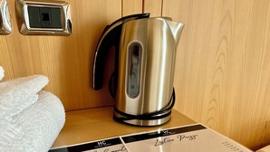 Ein Edelstahl-Wasserkocher auf einer Holzoberfläche, ein weißes Handtuch und eine Speisekarte mit aufgeführten Hotelservices.