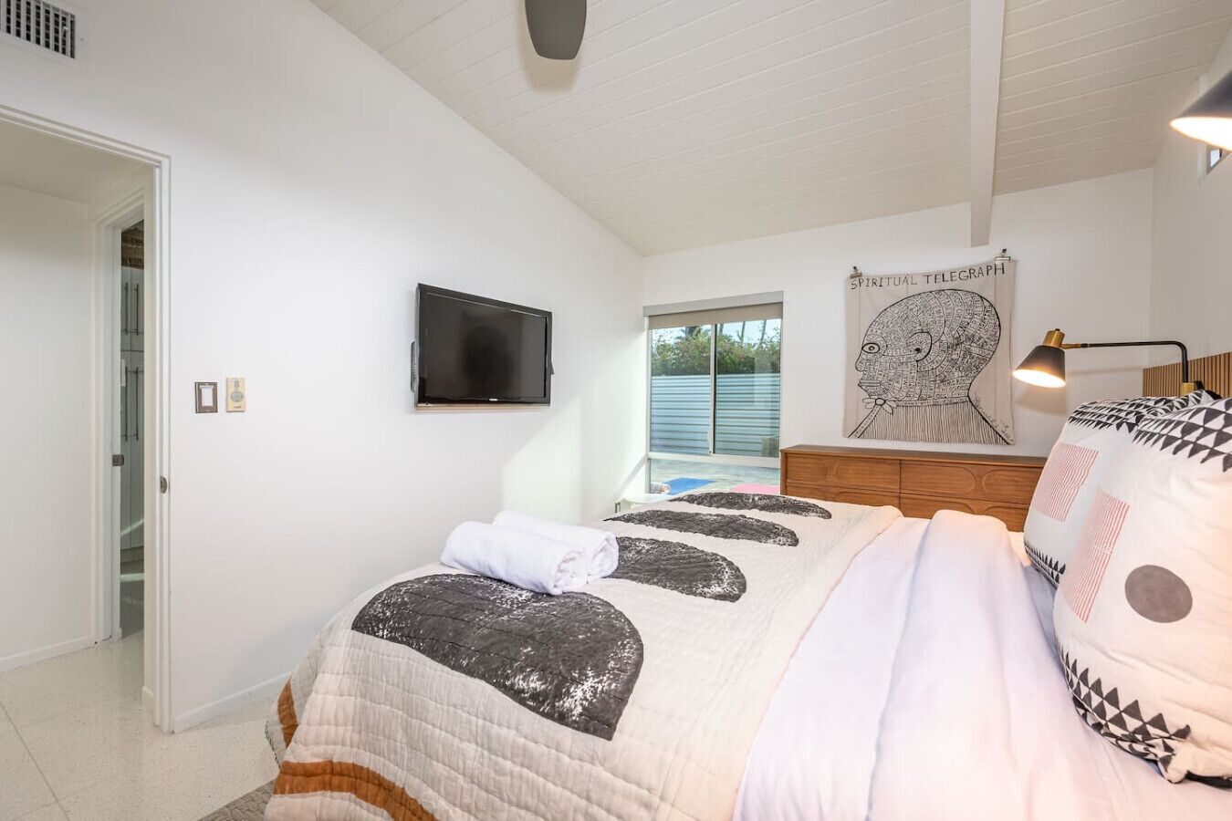 A bedroom with a bed, a television, a window, and a wall-mounted artwork.