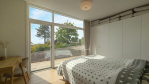 A bedroom with a large window, a bed with a star-patterned blanket, a wooden desk, and a chair. - Beautiful home in Knebel with sauna (Knebel)