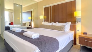 Habitación de hotel con una cama grande, cabecera de madera, dos lámparas de noche, una mesita de noche y un espejo amplio.