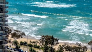 Un edificio de gran altura con varios balcones que dan a una playa con olas y un cielo azul despejado.