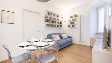 Un soggiorno moderno con un tavolo da pranzo apparecchiato per quattro persone, un divano blu e scaffali a parete con libri e oggetti decorativi.