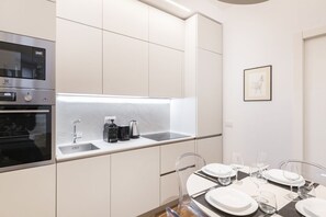 A modern kitchen with built-in appliances, a dining area with a table set for four, and a framed picture on the wall. - Easylife - Milano - Tadino 6 - Porta Venezia (Milano)