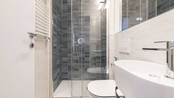 Un bagno moderno con doccia vetro, water bianco e un ampio lavandino bianco.