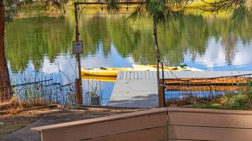 A wooden bench and a fire pit by a calm lake with a dock and a sign.