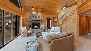 A log cabin interior with a stone fireplace, wooden staircase, and a cozy seating area. - Risa Cabin: Hot Tub, Private Lake (Bend)