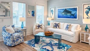 Un salón con un sofá blanco, un sillón estampado, una mesa de centro y obras de arte que representan la vida marina.