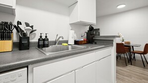 Eine moderne Küche mit grauer Arbeitsplatte, weißen Schränken, einem Spülbecken und einem Essbereich mit Tisch und Stühlen.