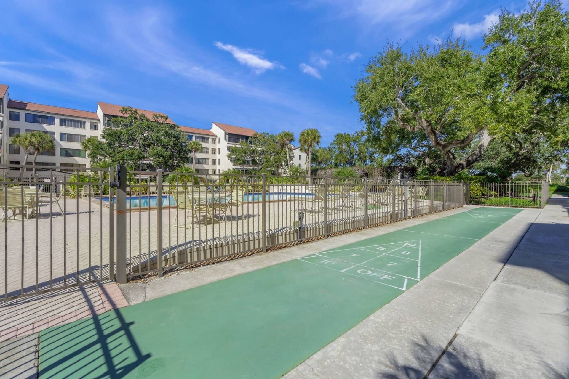 A courtyard with a shuffleboard court, a pool, and a fenced area with lounge chairs.