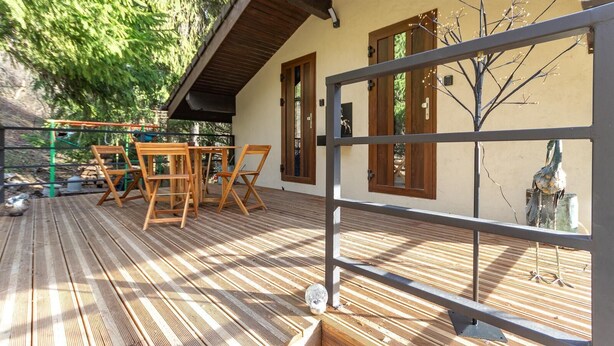 Un terrazzo in legno con mobili da esterno, una pergola e vista su un uccello alla finestra.