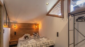 Una camera da letto con soffitto spiovente, una testiera in legno, due lampade ai lati del letto, un letto con una coperta soffice e un armadio in legno con attaccabiti.