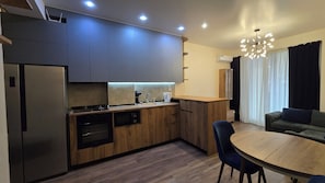 Eine moderne Küche mit eingebauten Geräten, ein Essbereich mit Holztisch und -stühlen sowie ein Wohnzimmer mit Sofa und einer Deckenleuchte.