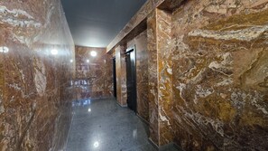 Un pasillo con suelo de mármol, una lámpara en el techo y una puerta al final.