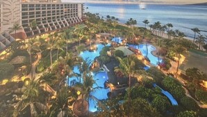 Un complexe hôtelier doté d’une grande piscine entourée de palmiers et offrant une vue sur l’océan.