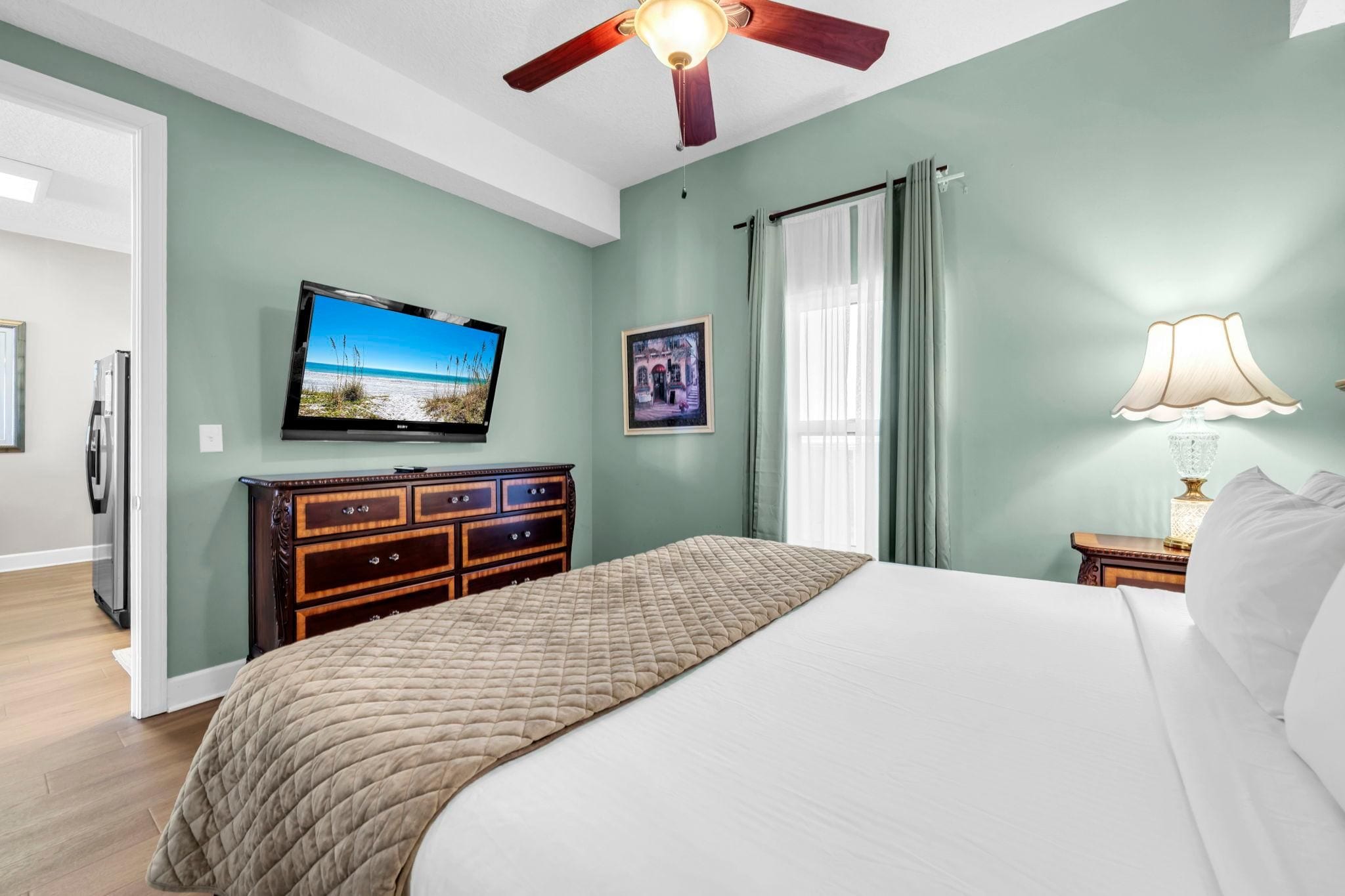 Ein Schlafzimmer mit Bett, Fernseher, Kommode, Lampe und Deckenventilator.