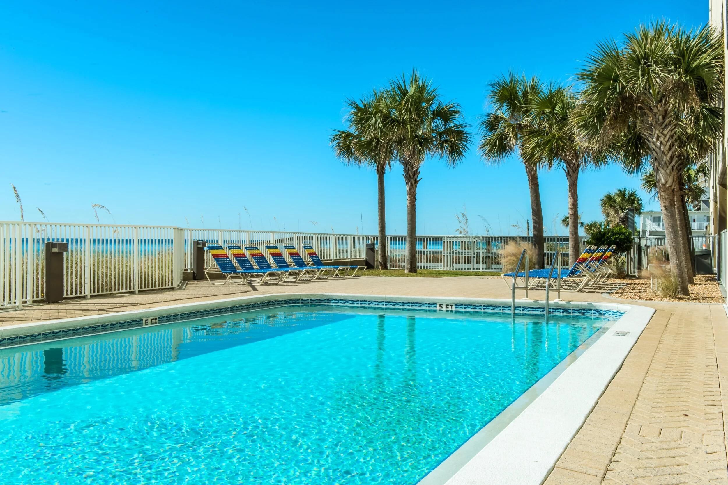A clear blue pool with lounge chairs and palm trees.