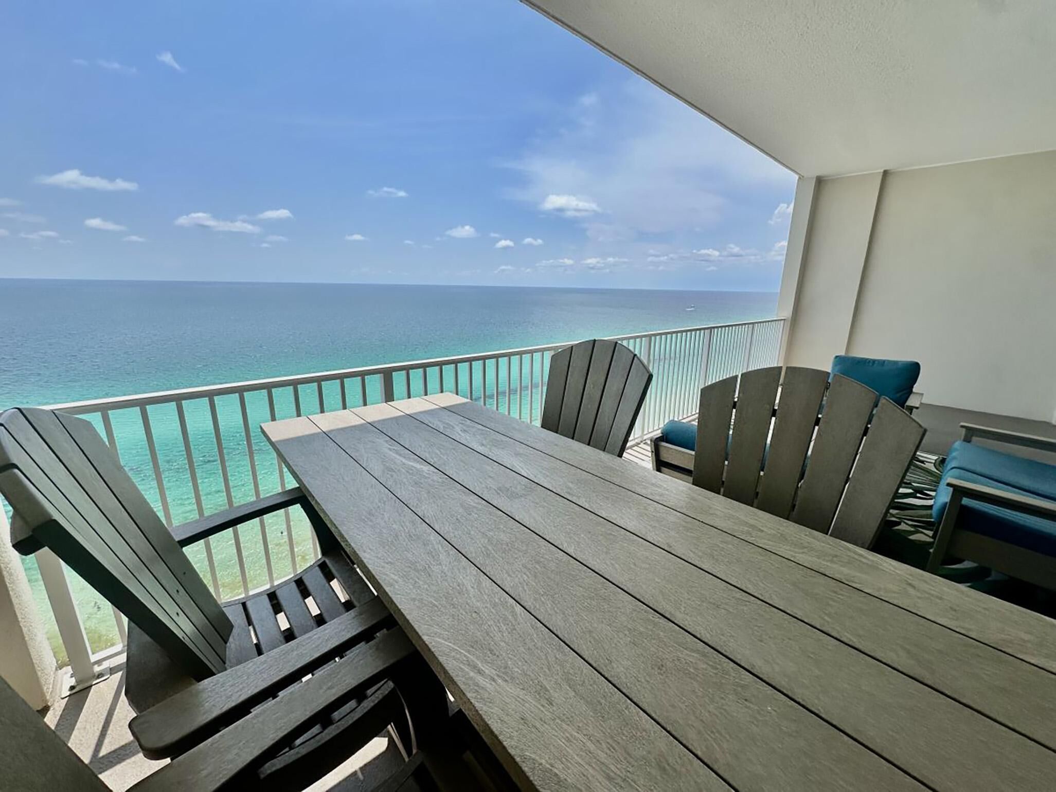 A balcony with a wooden table and chairs, overlooking a turquoise sea.