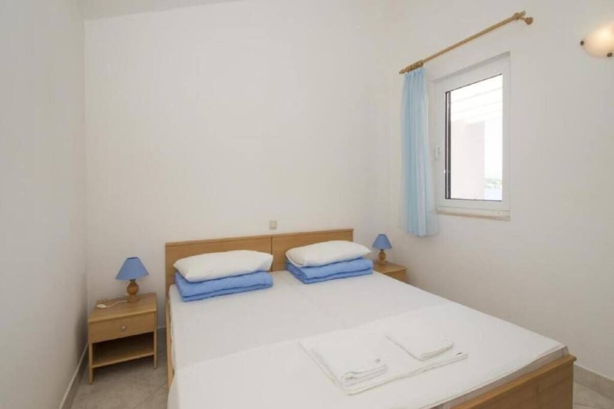Een slaapkamer met een bed, twee nachtkastjes, een raam met gordijn en een wandlamp.