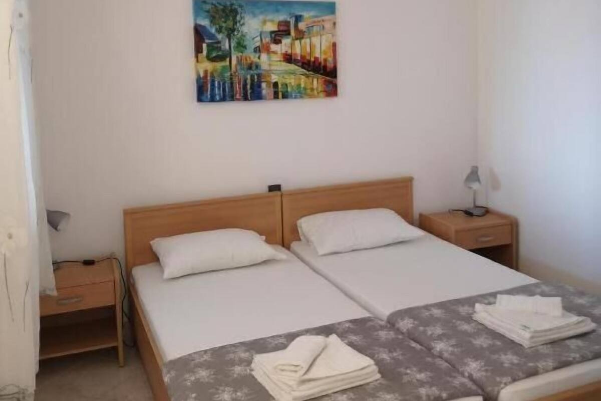 Een tweepersoonsbed met een houten hoofdbord, twee nachtkastjes en een schilderij aan de muur.