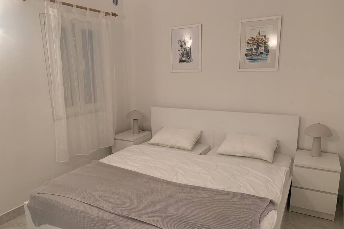 Een slaapkamer met een bed, twee nachtkastjes, een raam met dunne gordijnen en twee ingelijste foto's aan de muur.