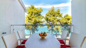 A balcony with a table and chairs, a bowl of fruit, and a view of trees and water. - Lumbarda Resort Apartments (Lumbarda)