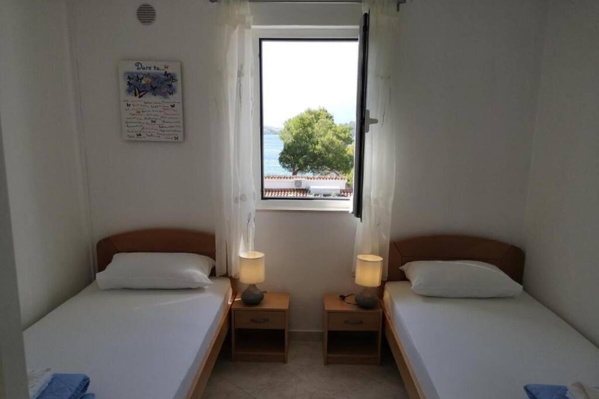 Een kleine, schone kamer met twee enkele bedden, een raam met uitzicht op zee en een bordje aan de muur.