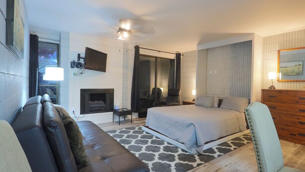 Een slaapkamer met een bed, een bank, een televisie, een open haard en een spiegel.