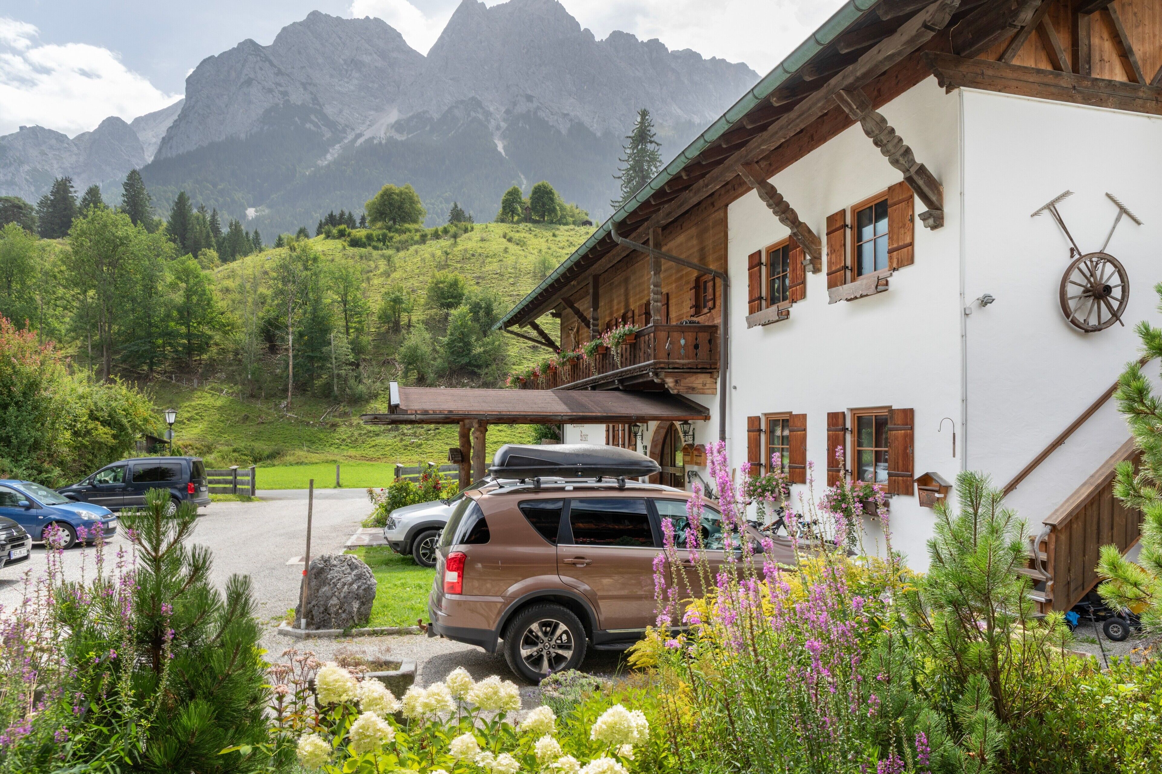 A mountain lodge with a parking area, a wooden building with a balcony, and a bicycle mounted on the wall.