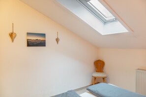 A bedroom with a skylight, a bed, a chair, and wall-mounted decorations.