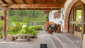 A wooden covered porch with stone flooring, a rustic fence, and a view of a green hillside. - Apartment Kramer with Mountain View and Wi-Fi (Grainau)