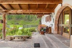 Eine hölzerne Veranda mit Steinböden, einem rustikalen Zaun und Blick auf einen grünen Hang.