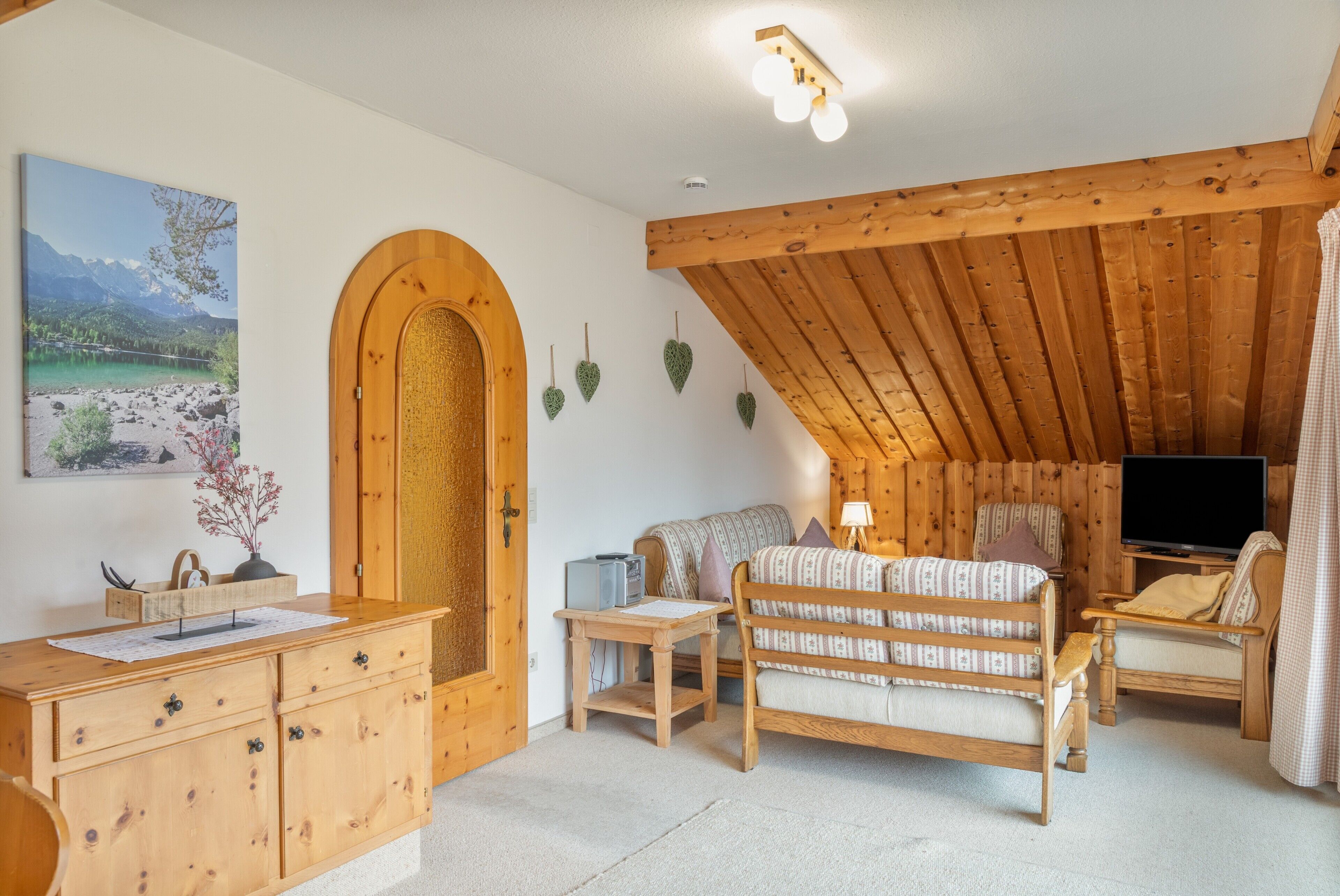 Ett mysigt rum med ett träpanelat tak, en soffa, en tv och ett skrivbord med lådor.
