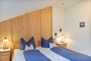 A bedroom with a wooden headboard, two bedside tables with lamps, and a bed with blue bedding. - Apartment 'Waxenstein' with Mountain View, Balcony and Wi-Fi (Grainau)